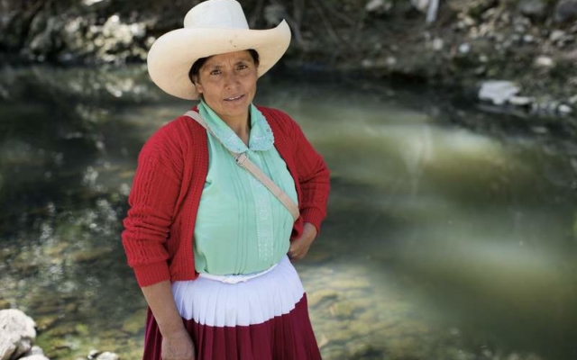 an image of Maxima Acuna. She is wearing a large white wide brimmed hat, a red cardigan, green shirt and a white and red skirt. 