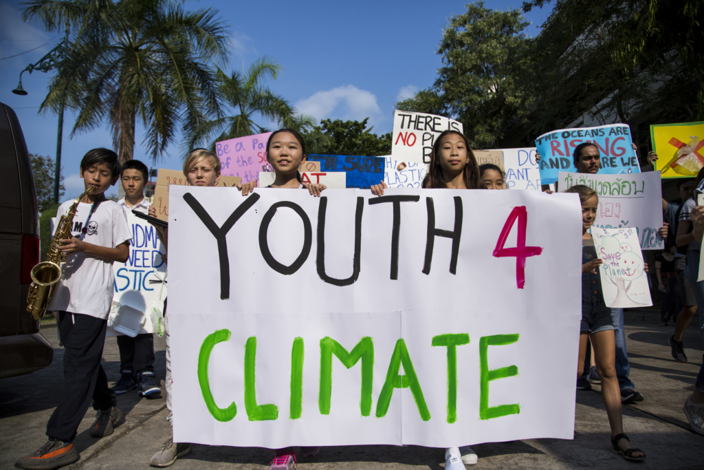 Marching students in Bangkok hold banners reading Youth 4 Climate