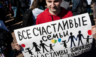 A protester in Russia bearing a poster saying "All happy families are equally happy", a quote by Leo Tolstoy, and depicting heterosexual and homosexual families with kids
