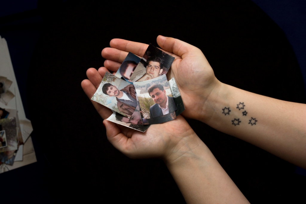 someone is holding a collection of images of people who have disappeared in Syria. The person has a star tattoo on their left hand. 