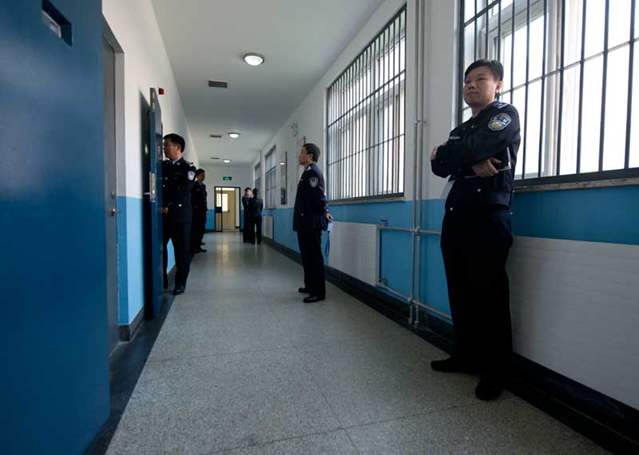 Police guards stand in a hallway inside the No.1 Detention Center in Beijing. The walls are painted blue and white.